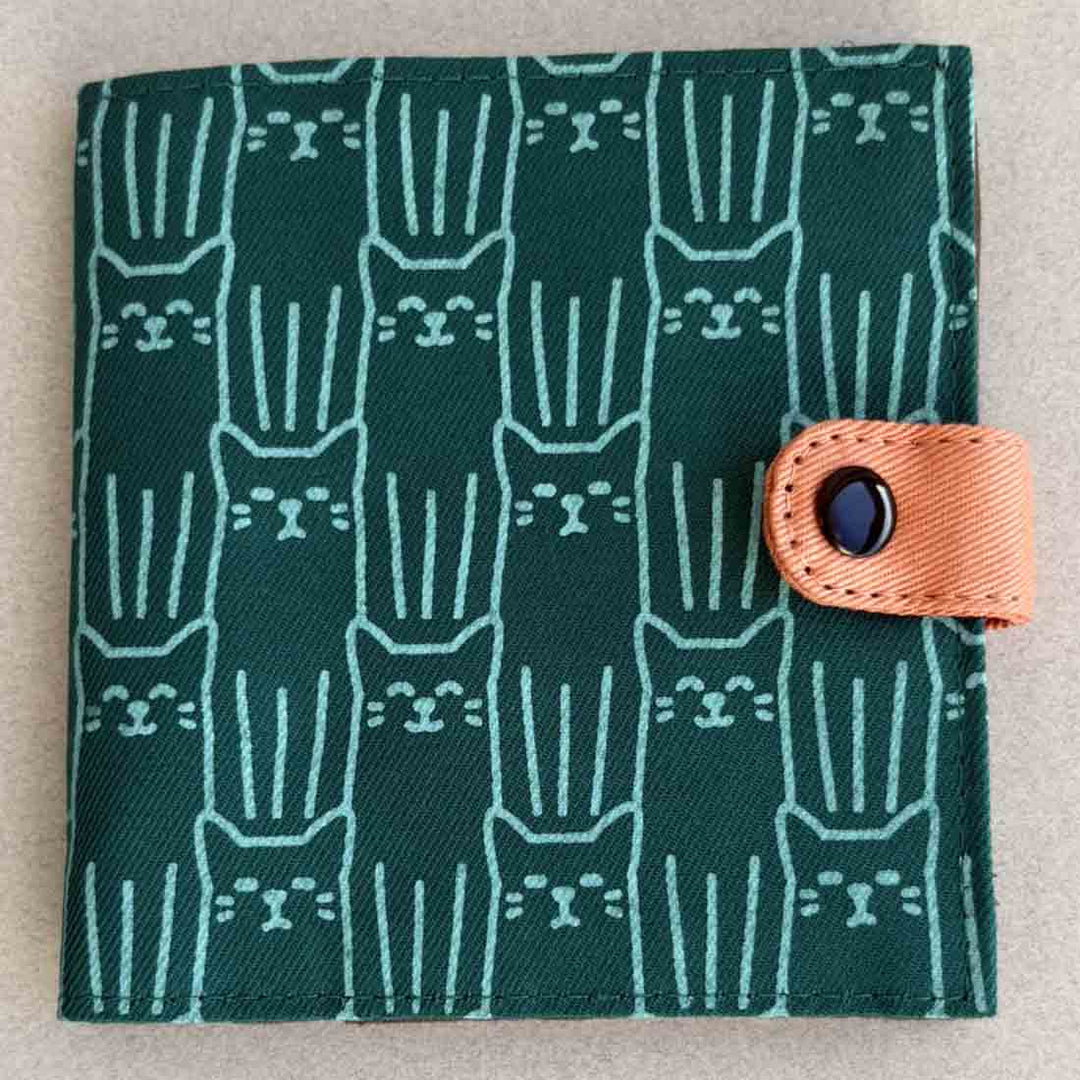 Green fabric wallet with cat pattern and brown strap on a beige background