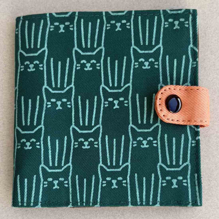 Green fabric wallet with cat pattern and brown strap on a beige background
