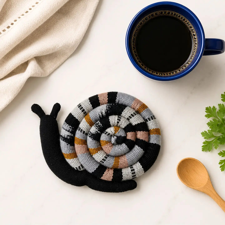 Snail-shaped trivet with multicolor pattern on a white surface next to a blue mug of coffee.