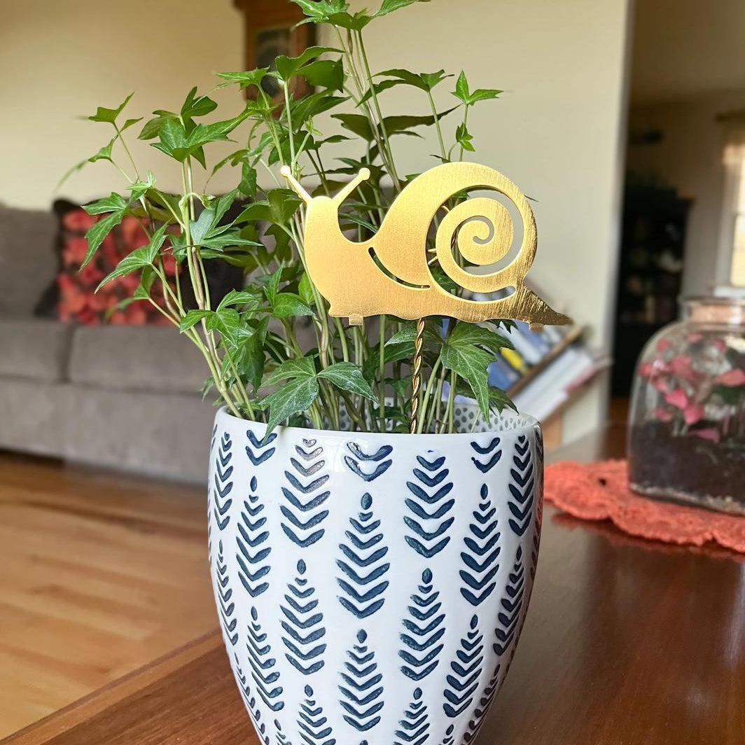 Potted plant with a decorative snail stake on top in a room setting