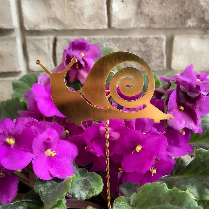 Decorative snail ornament among purple flowers against a brick wall background