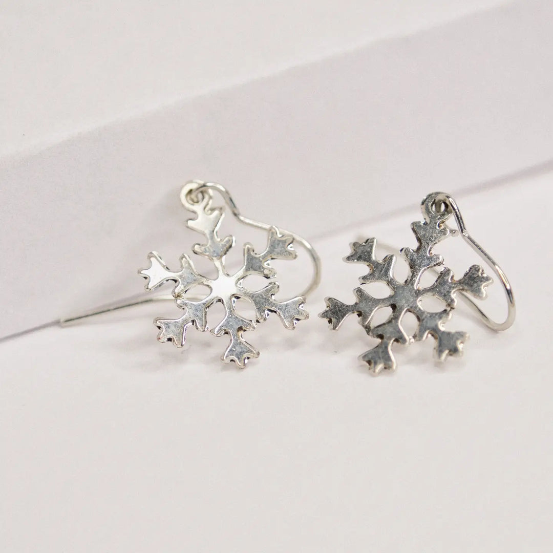 A pair of silver snowflake-shaped dangle earrings with fishhook backs, displayed on a clean white surface.