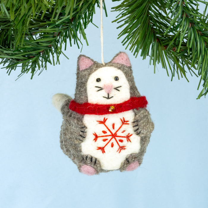 Cat-shaped Christmas ornament with a red snowflake design hanging on a tree branch.