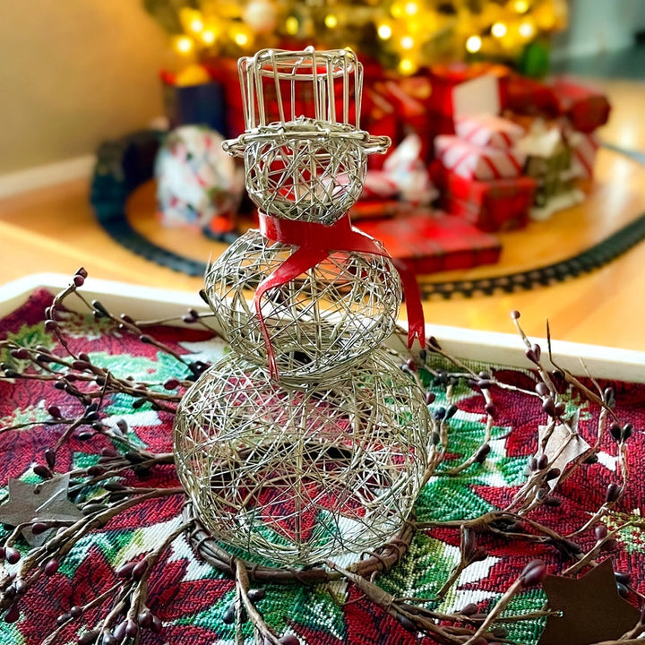 Decorative silver snowman on a Christmas-themed tablecloth with blurred festive background.