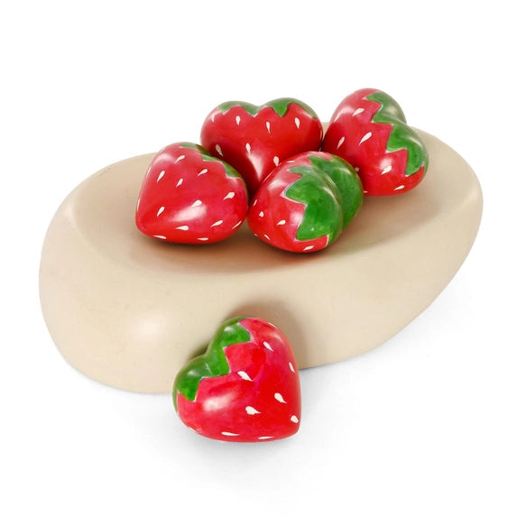 Five heart-shaped soapstone strawberries in red and green, displayed on a beige oval wooden tray against a white background.