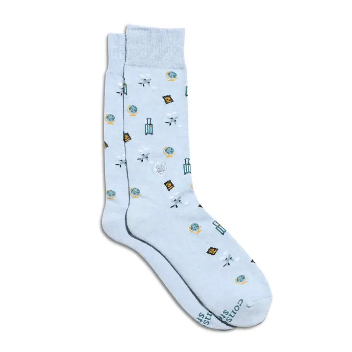 A pair of light blue crew socks with a small, scattered pattern of travel-themed icons such as suitcases, airplanes, and maps. The brand name 'COOL SOX' is printed in dark blue near the toe of the front sock.