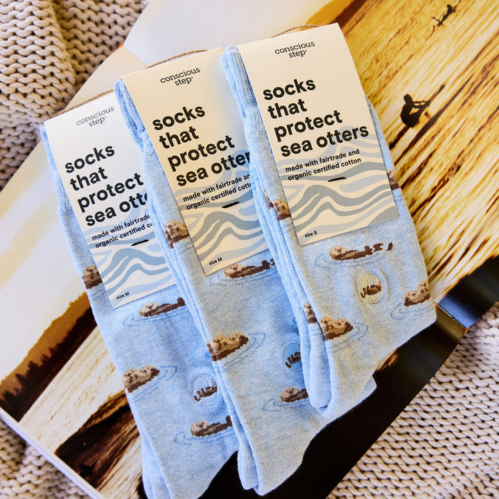 Three pairs of socks with sea otter design and 'conscious step' branding on a wooden surface.