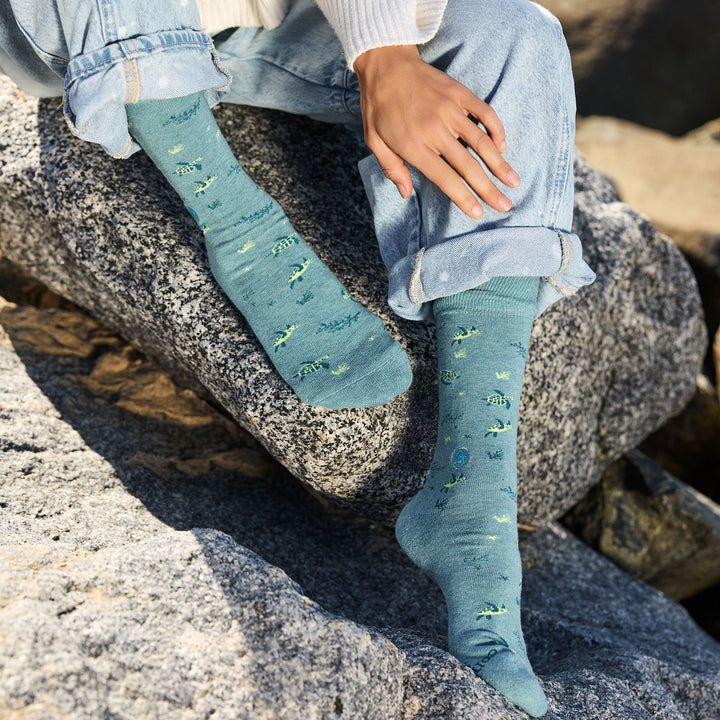 Person wearing blue sea turtle patterned socks sitting on rocks