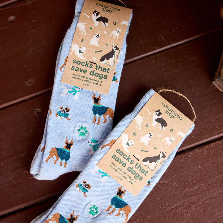 Two pairs of socks with dog-themed design on a wooden surface, featuring 'conscious step' branding.