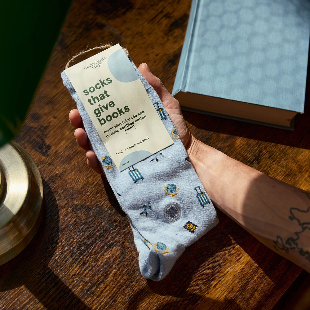 Person holding a sock with 'socks that give books' packaging on a wooden surface