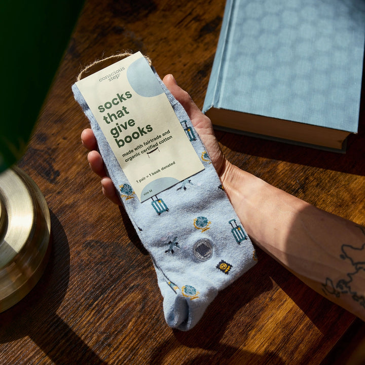 Person holding a sock with 'socks that give books' packaging on a wooden surface