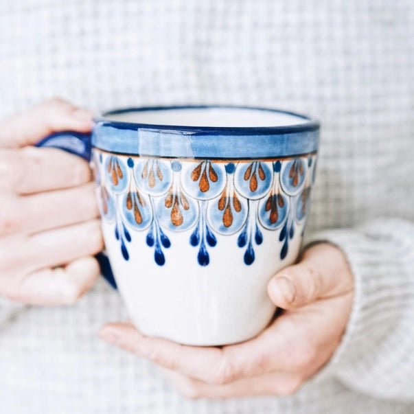 Person holding a ceramic mug with blue and brown decorative patterns against a neutral background