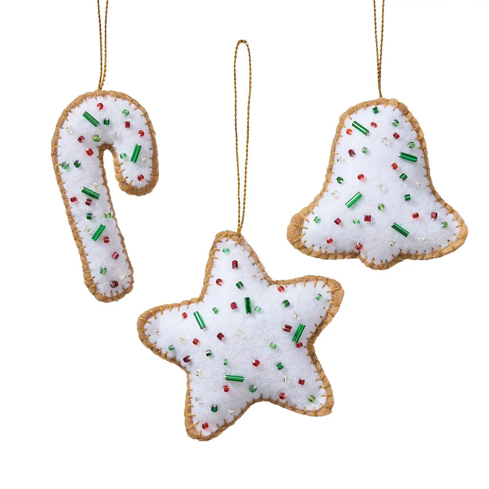 Three white felt Christmas ornaments shaped like a candy cane, bell, and star, decorated with red and green sprinkles and hanging by gold-colored strings on a white background.