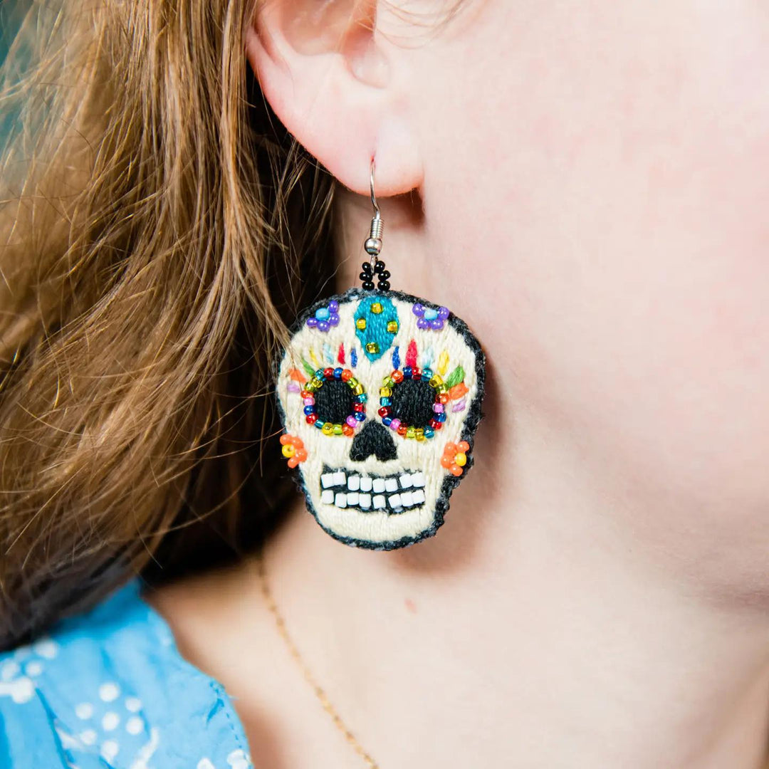Colorful skull-shaped earrings worn by a person with a blurred background