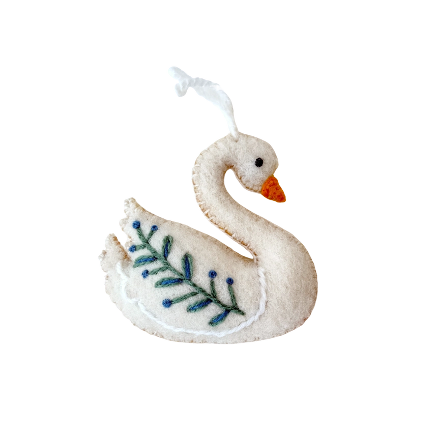 A white felt swan ornament with a small orange beak, embroidered blue leaf pattern on its side, and a white hanging loop at the top, shown on a plain white background.