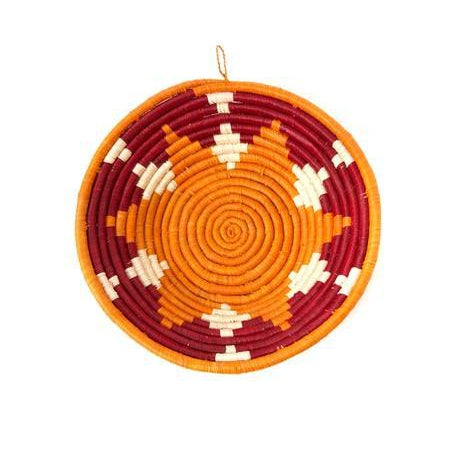 A handcrafted Ugandan sweet potato and sorghum raffia coil basket with a red and beige geometric pattern, suitable for wall or table decor.