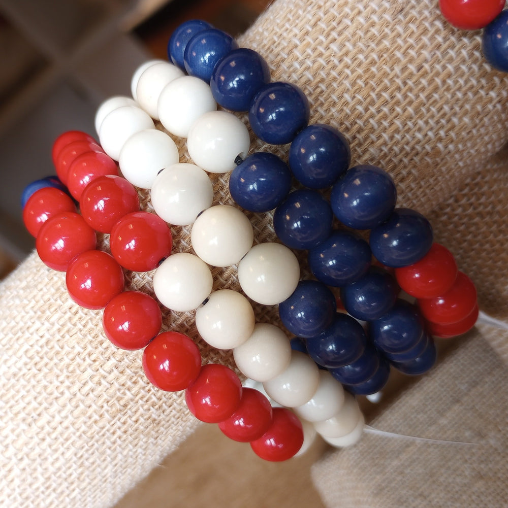 Three beaded bracelets in red, white, and blue on a textured surface.