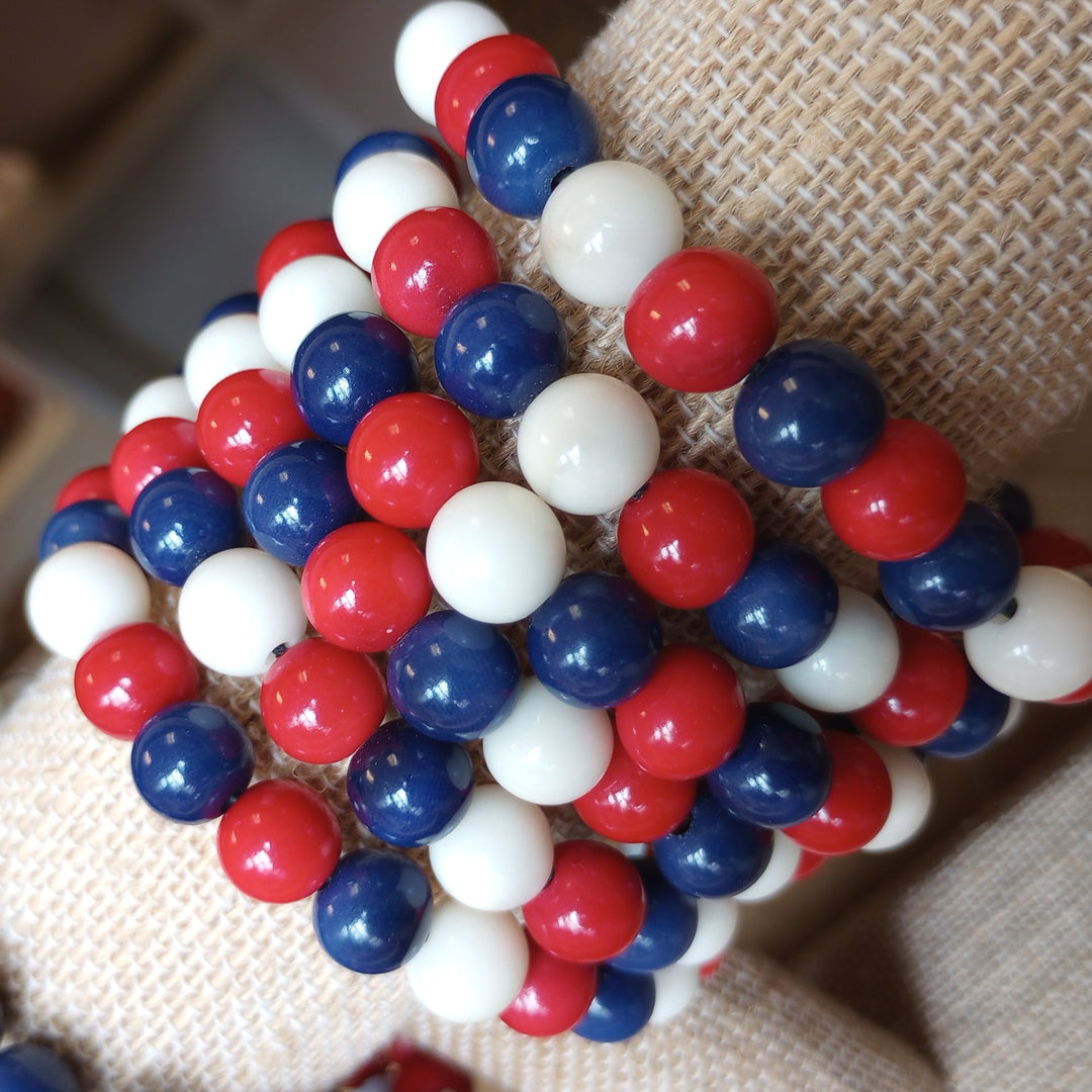 Close-up of a bracelet with red, white, and blue beads on a textured fabric background
