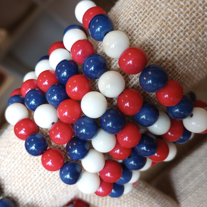 Close-up of a bracelet with red, white, and blue beads on a textured fabric background