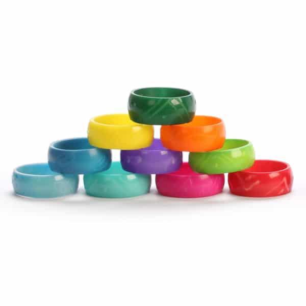 A collection of colorful handmade tagua rings in various shades of green, blue, pink, and red, stacked together.