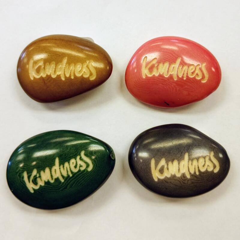 Four colorful tagua nut with 'Kindness' engraved on them against a white background