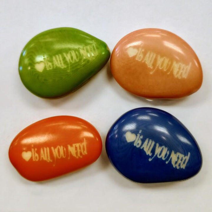 Four colorful tagua nuts with 'love is all you need' text on a white background