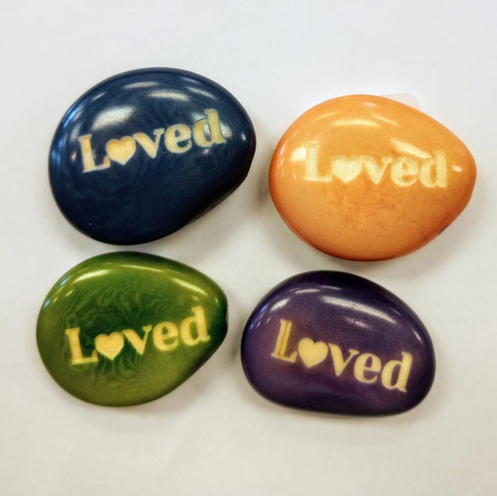 Four colorful tagua nuts with 'Loved' text on a white background