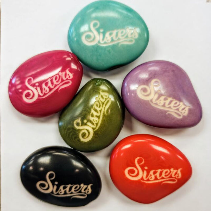 Colorful tagua nuts with 'Sisters' engraved on a white background