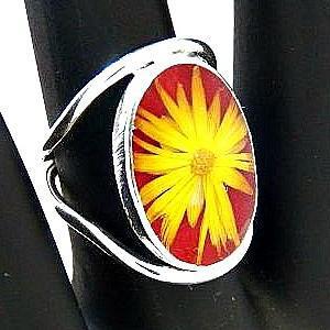 A silver metal ring set with a resin-enclosed flower on a display hand.