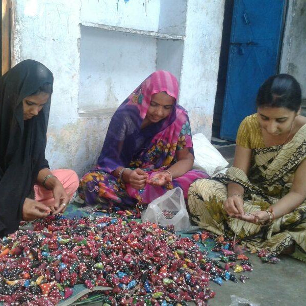 Three women sitting on the ground sorting colorful beads.