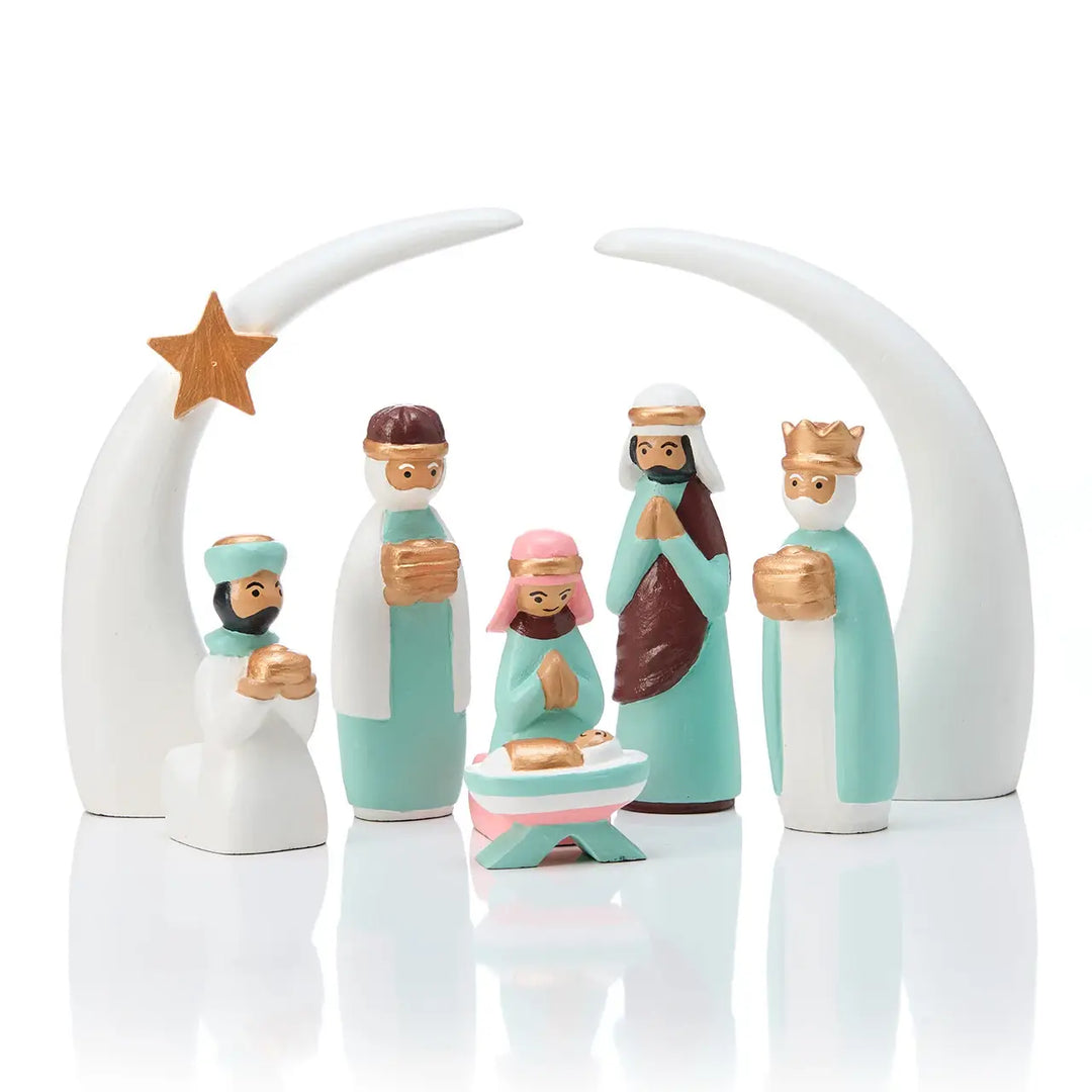 A nativity scene figurine set featuring baby Jesus in a manger with Mary, Joseph, three wise men, and a star under a white crescent moon arch on a reflective white surface.
