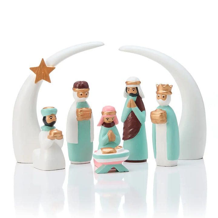 A nativity scene figurine set featuring baby Jesus in a manger with Mary, Joseph, three wise men, and a star under a white crescent moon arch on a reflective white surface.