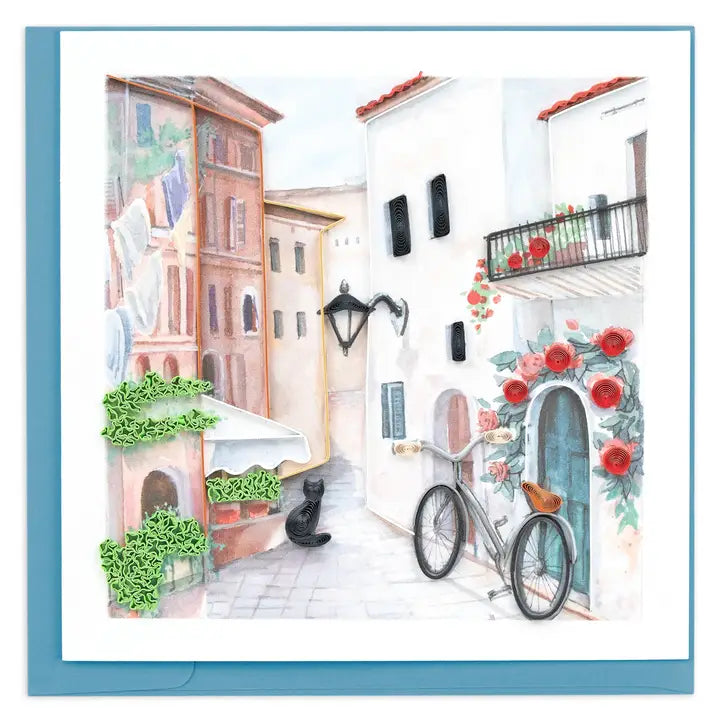 A square art print or card featuring a watercolor-style illustration of a narrow white building street with red flowers, a bicycle, green ivy, and a black cat, set against a light blue border.