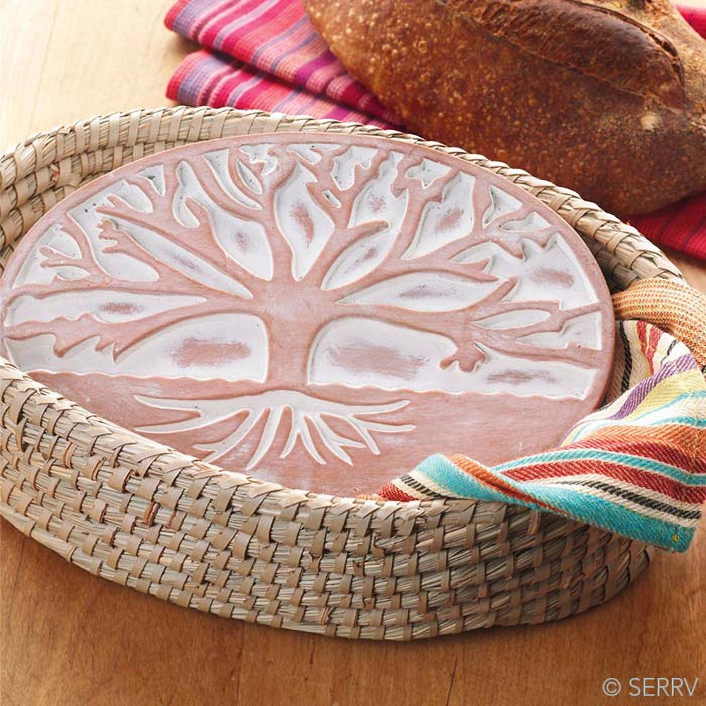 warming plate with tree design on a woven tray, surrounded by bread and colorful napkins.