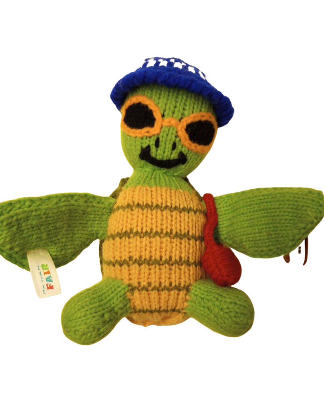 Knitted turtle toy with sunglasses and a blue cap on a white background