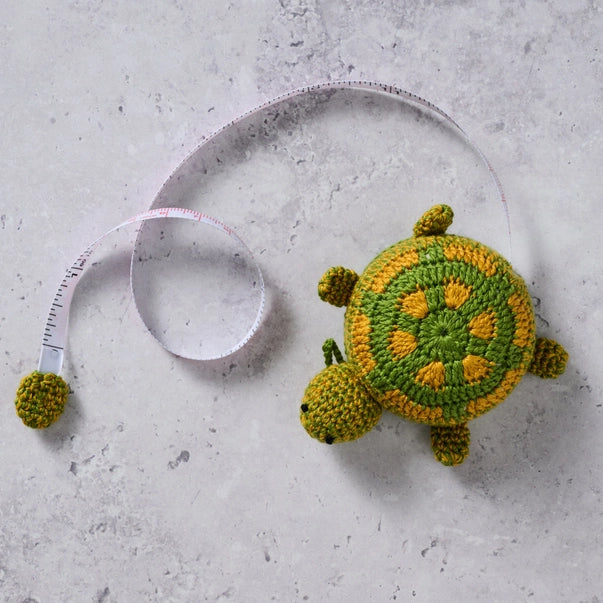 Crocheted turtle  measuring tape on a concrete surface