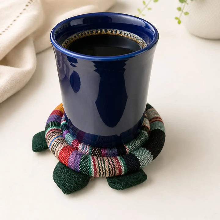 Blue mug with a colorful turtle-shaped woven coaster on a white surface.