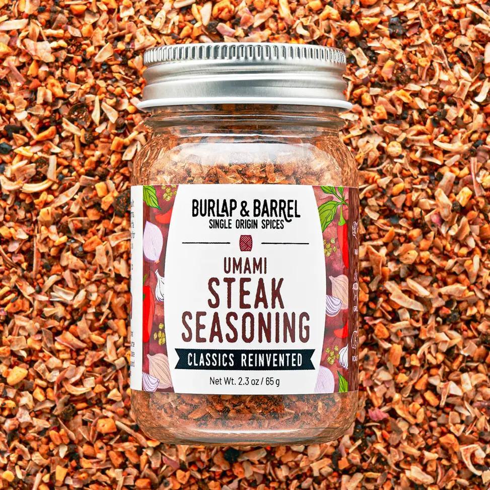 Jar of Burlap & Barrel Umami Steak Seasoning on a background of spices