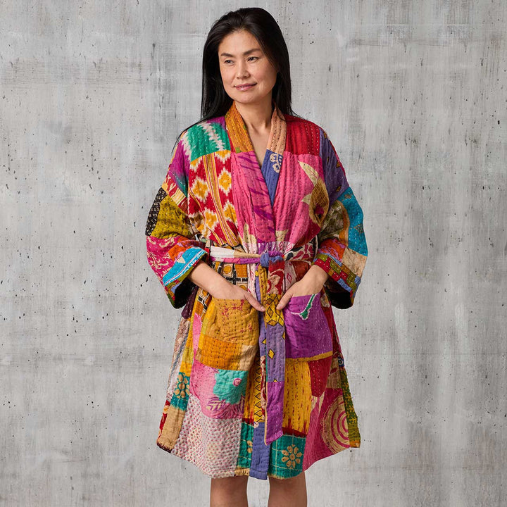 Woman wearing a colorful patchwork robe against a gray concrete wall