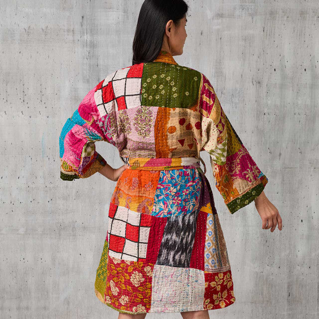 Woman wearing a colorful patchwork robe against a concrete wall.