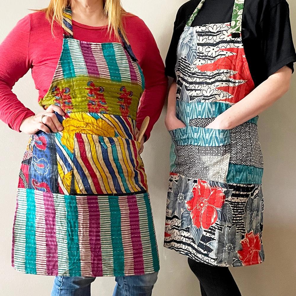 Two people wearing colorful upcycled kantha aprons with various geometric and floral patterns.