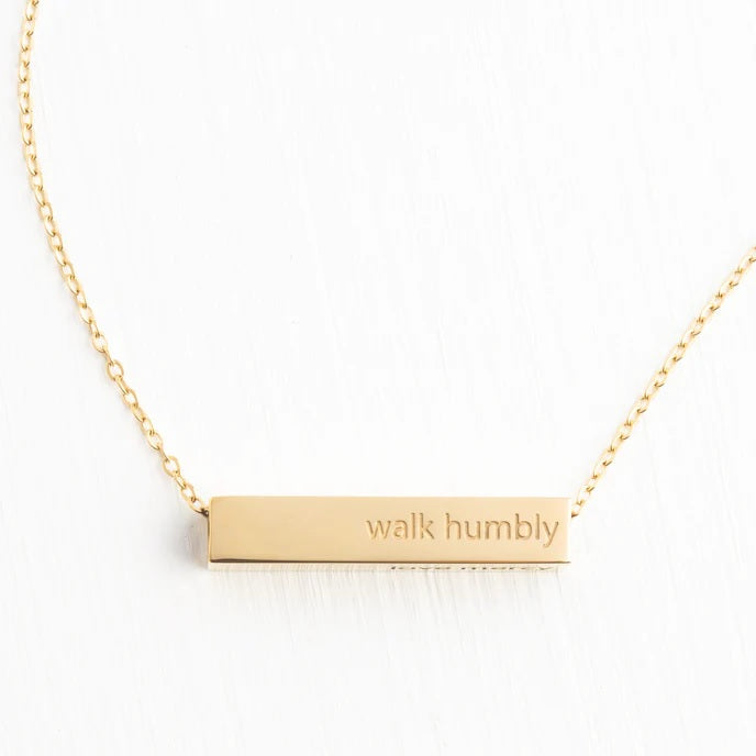 Gold necklace with 'walk humbly' pendant on a white background