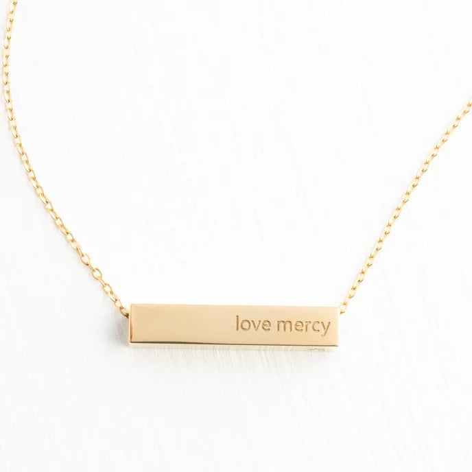 Gold necklace with 'love mercy' pendant on a white background