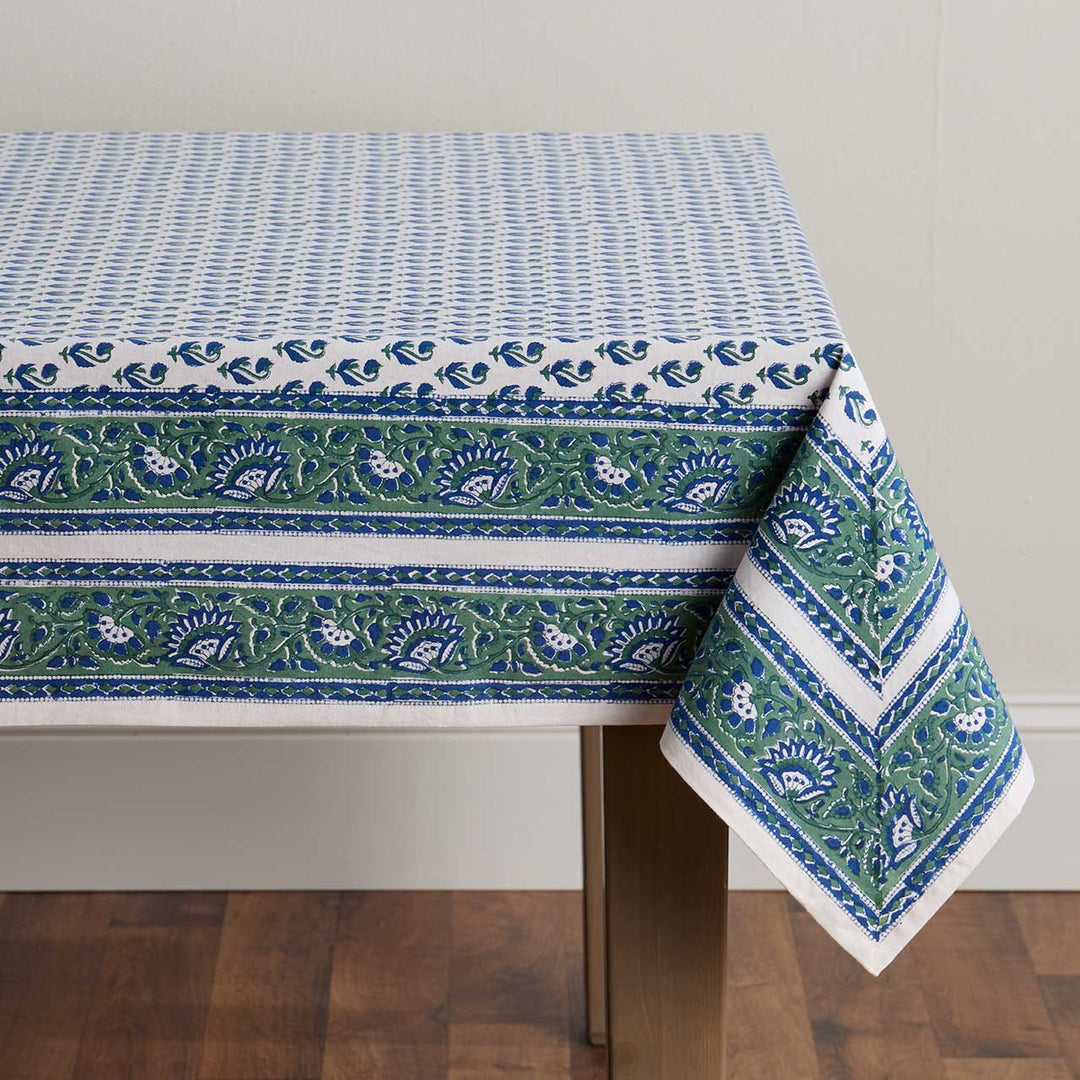 Block print tablecloth with blue and green pattern on a wooden table against a gray wall.