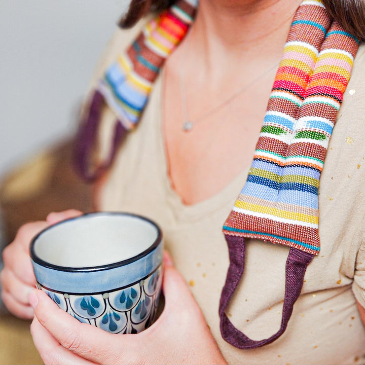 Person holding a ceramic mug with a colorful striped neck wrap over shoulder