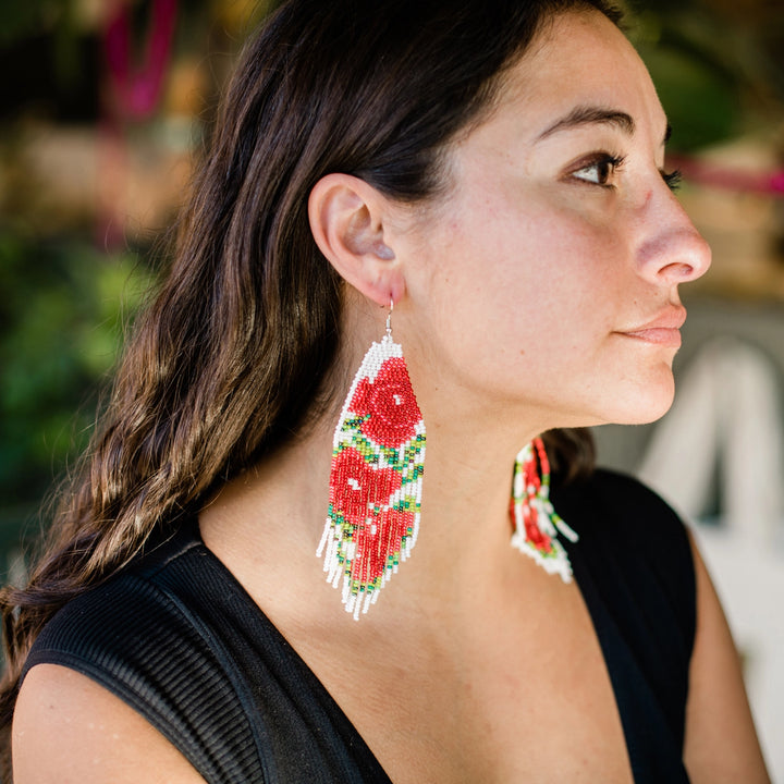 Woman wearing red and green and white beaded earrings with a blurred background