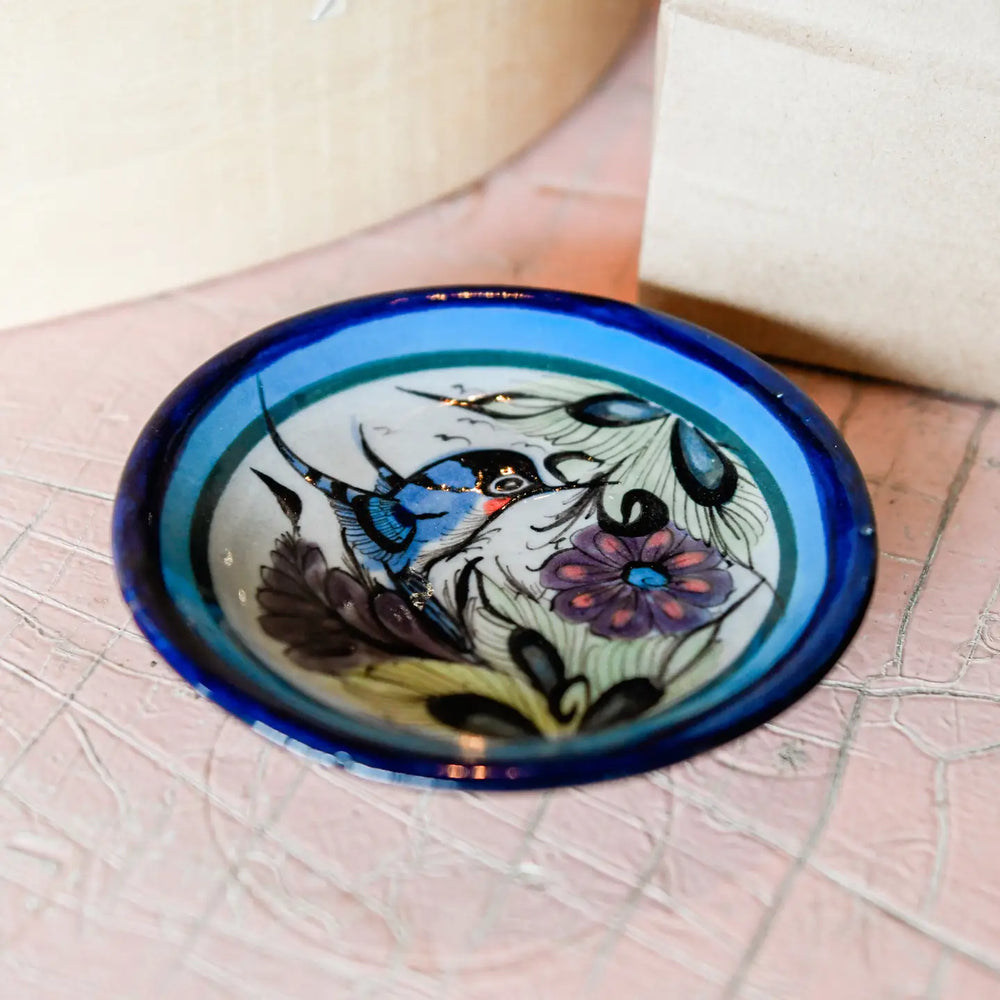 Decorative glass bowl with hummingbird and floral design on a textured surface