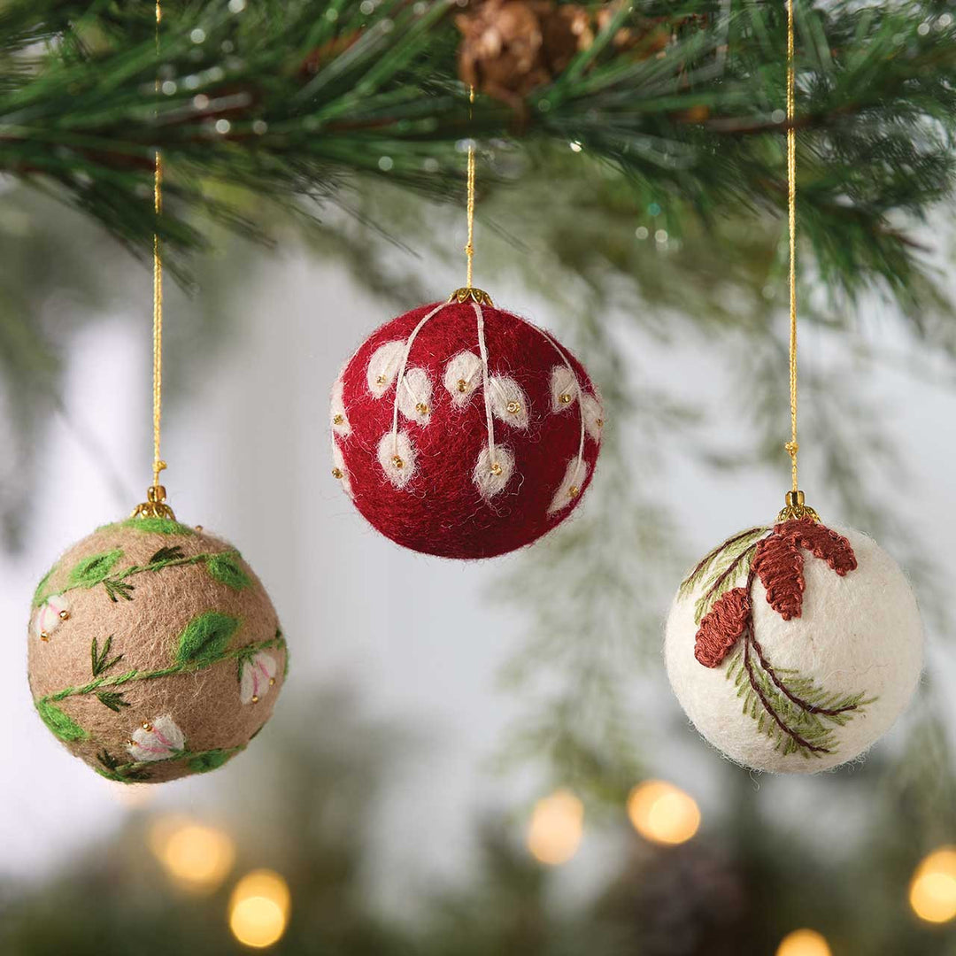 Three decorative Christmas balls hanging on a tree branch with blurred lights in the background.