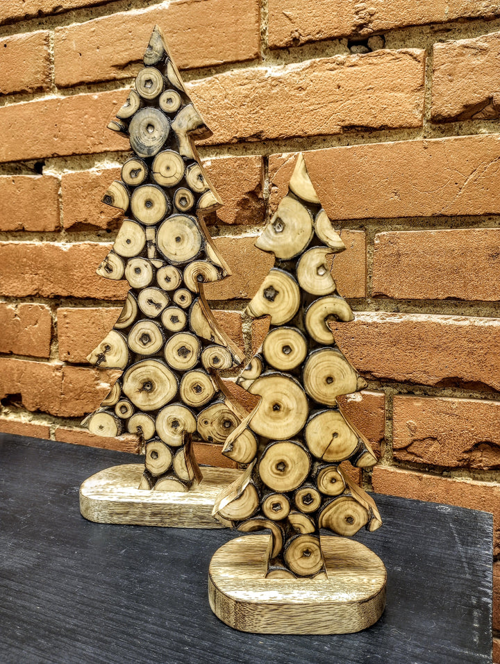 Two decorative wooden Christmas trees made from stacked log slices, displayed on a dark tabletop against a rustic red brick wall.