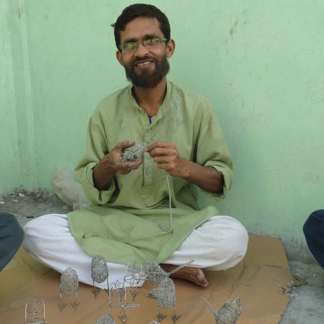 Man sitting on the floor with wire sculptures in front of him against a green wall.